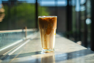 A glass of iced coffee and milk cream on a stone table in a coffee shop with a contrast combination of sunlight from the window and shadow. Bokeh background.