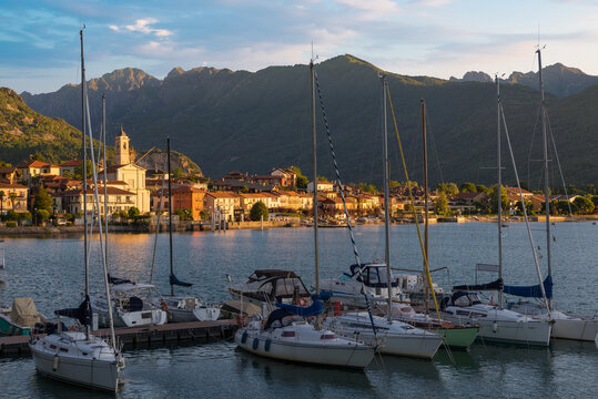 Lakeside town lit by the rising sun, with sailing boats in the foreground. Lake Maggiore in Feriolo in a beautiful summer morning, Italy