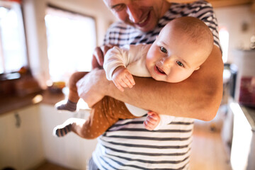 Handsome dad holding small baby, carrying him around house. Unconditional paternal love, father's...