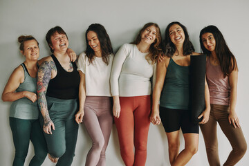 Laughing group of young women in sportswear leaning against the wall of yoga studio after a class together