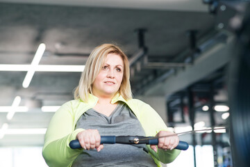 Overweight woman exercising on rowing machine. Routine workout for physical and mental health