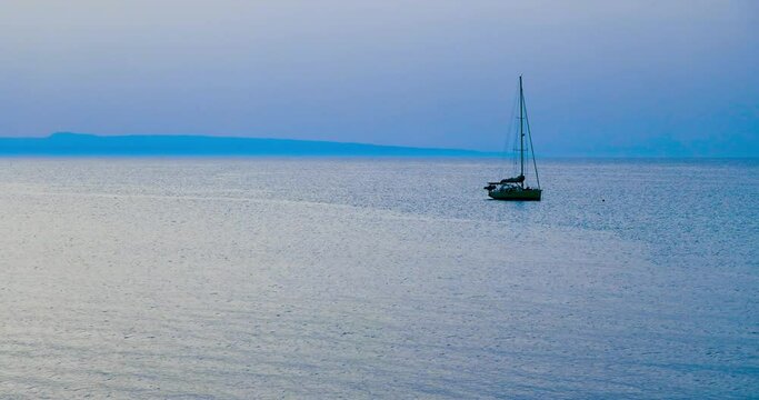  Barca a vela alla fonda in mare calmo con promontorio del Gargano (Puglia) sullo sfondo con cielo nuvoloso