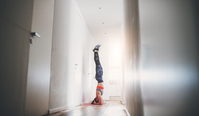 Beautiful redhead woman doing headstand during home fitness routine. Home workout on gym mt in living room, sporty woman wearing sportswear.