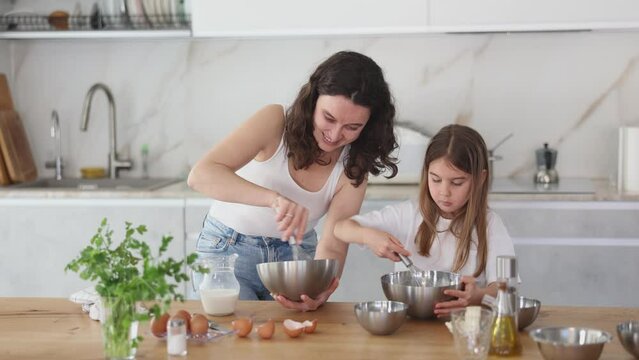Happy mother and her daughter whisking ingredients in a bowl using metal corolla in the kitchen