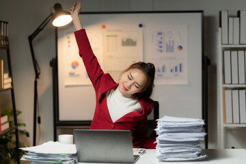 Late Night Hustle: A determined businesswoman stretches at her desk, surrounded by paperwork and a...