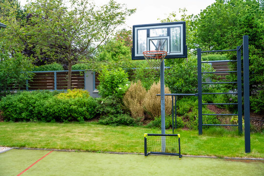 Basketball hoop, portable soccer goal, and pull-up bar in a backyard garden during the day - Powered by Adobe
