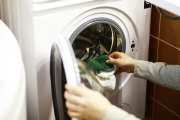 Person Loading Washing Machine with Green Cloth at Home