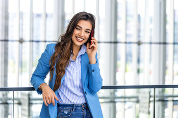 In a modern building, a confident businesswoman smiles while using her cellphone outside the office, radiating professionalism and contentment.