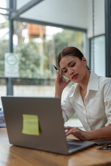 Tired, stressed Asian businesswoman suffering from headaches after using a laptop for a long time, female office worker sitting for a long time Office syndrome concept.