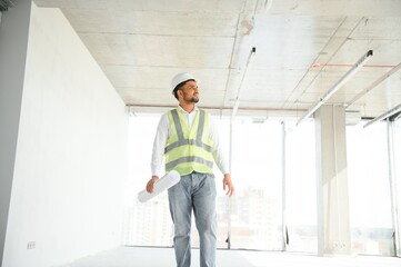 Indian construction site manager standing wearing helmet, thinking at construction site. Portrait of mixed race manual worker or architect