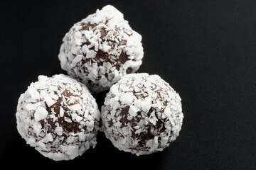 Three handmade chocolates sprinkled with coconut on a dark background. Photo. Macro. Selective focus