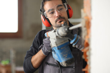 Construction worker is wrecking wall using rotary hammer