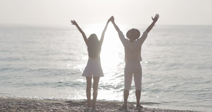 Joyful Couple Raising Hands on the Beach at Sunset