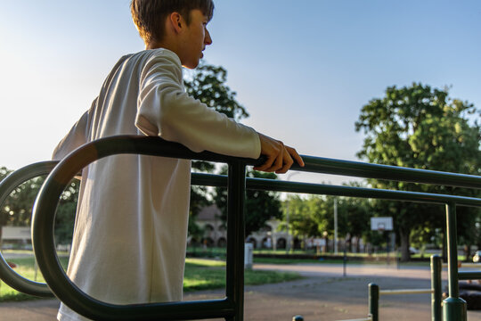 Young Man Leaning on Parallel Bars at Outdoor Park Workout Area