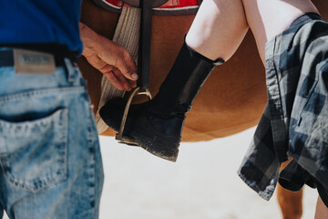 Close-up of a person helping a rider adjust the stirrup while mounting a horse, emphasizing...