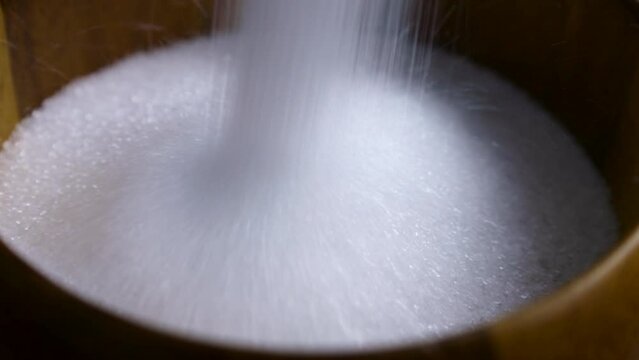 White natural organic sweet Erythritol sweetener granules falling down into the wooden bowl close up. Sugar substitute concept