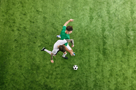 Aerial view. Dynamic photo of intense battle between two young men, soccer players for ball on green lush playground. Concept of professional sport, championship, final match, movement. Ad - Powered by Adobe