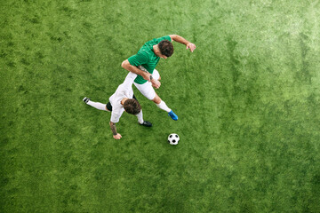 Fototapeta premium Aerial view. Two young me, soccer players competing for possession of ball on green lush playground. Concept of professional sport, championship, final match, movement. Ad