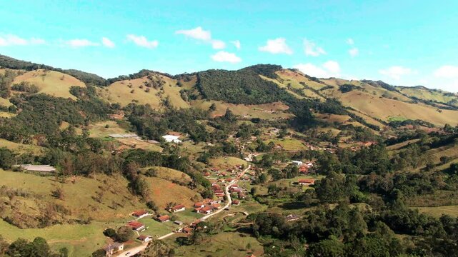A drone footage captures a breathtaking view of a small village located in a valley surrounded by rolling hills. Delfim, Moreira, Ros&aacute;rio Minas Gerais