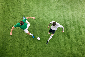 Aerial view. Two soccer players in attack position, fight for ball in motion on green lush playground. Concept of professional sport, championship, final match, movement. Ad