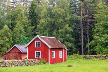 Red idyllic cottage with a stone wall by the forest edge
