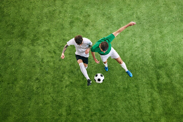 Aerial view. Two male soccer players compete for possession of ball on green lush playground. Concept of professional sport, championship, tournament, final match, movement. Ad