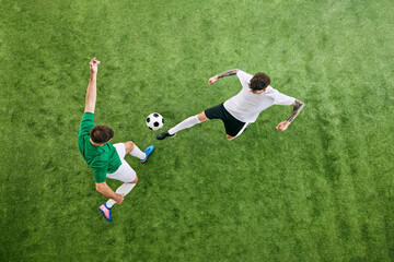 Aerial view. Two football athletes, one in white swings his leg, and other in green braces for play on lush playground. Concept of professional sport, championship, final match, movement. Ad