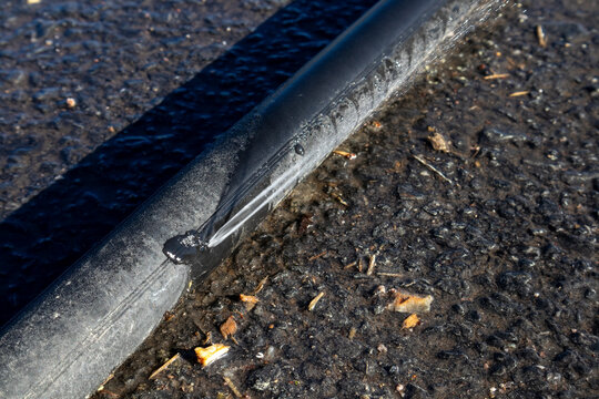 Leaking black polyethylene water pipe on ground outdoors