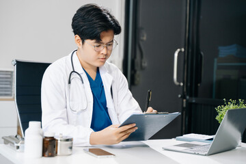 Confident young male doctor in white medical uniform sit at desk working on computer.