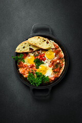 Tasty Breakfast Shakshuka in an Iron Pan. Fried eggs with tomatoes. On a black stone background.