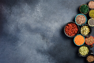 Set of superfoods, cereals, nuts and dried fruits, spirulina and goji in white ceramic bowls. On a gray concrete background. Top view. Free space for text.