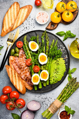 Nutritious Breakfast: green asparagus, avocado, chicken eggs and bacon. In a stone plate.