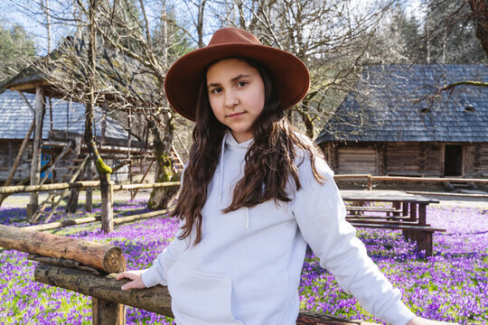 Smiling girl wearing hat and standing near purple flowers at farm