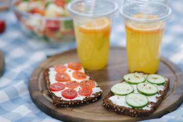 Vegan sandwiches on wooden board outdoors. Orange lemonade in disposable cups