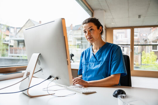 Young female nurse tying on keyboard of computer in clinic