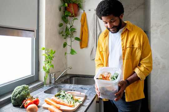 Afro man collecting compost in kitchen at home