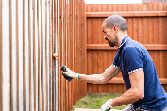 Man painting with paint roller on wooden fence