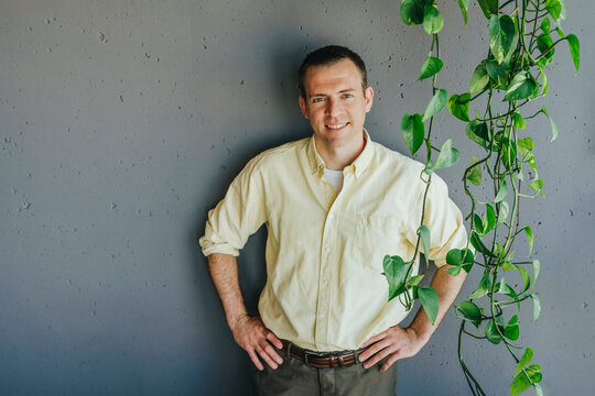 Smiling businessman standing with hands on hip in front of gray wall