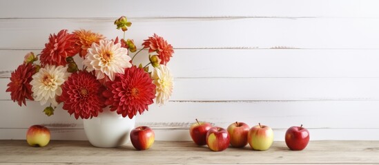 Indoor shot featuring exquisite chrysanthemum flowers in a pot and ripe apples neatly arranged on a white wooden table leaving room for textual additions. Creative banner. Copyspace image