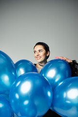 A stylish birthday girl with short dyed hair delicately holds a bunch of vibrant blue balloons.