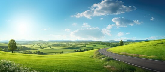 Obraz premium The copy space image shows a sunny scene with a blue sky green hills and a country road where the sun is directly shining towards the camera