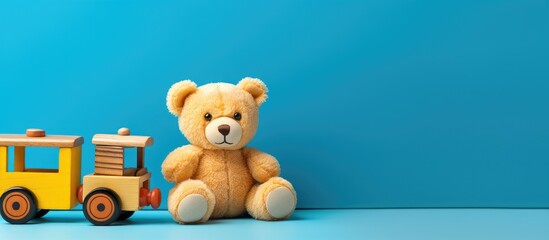 A copy space image of a baby kids toys frame featuring a charming teddy bear a wooden toy train a car and vibrant cubes set against a blue and yellow background