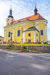 Naklejka premium The Church of St. Bartholomew in Pecka, Czechia, is a beautiful example of Baroque architecture. The yellow building features two spires and stands on a hill overlooking the town.