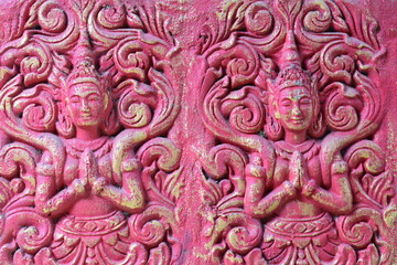 Bas-relief of a goddess with her hands folded on her chest in pink tones close-up.