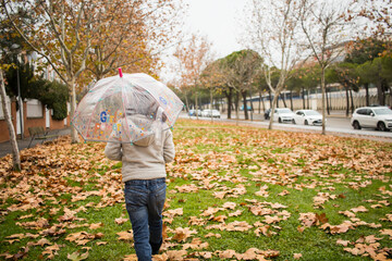 girl with umbrella walking at the rain in city autumn park, back view with copy space. Horizontal