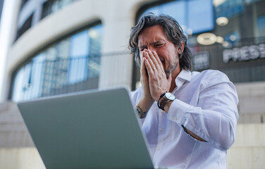 Portrait of mature businessman working on laptop outdoor, recieving bad news. Handsome man with...