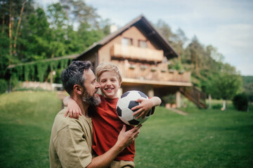 Dad embracing young son, running and celebrating the win after goal. Playing football on a lawn in...