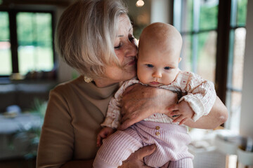 Lovely grandmother holding little baby in arms, looking at her lovingly. Strong bond between grandparent and grandchild.