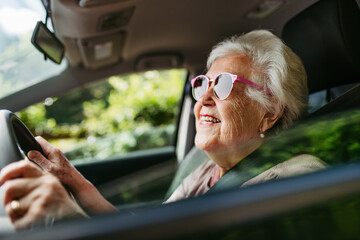 Happy senior woman driving car alone, enjoying car ride. Safe driving for elderly adults, older driver safety.