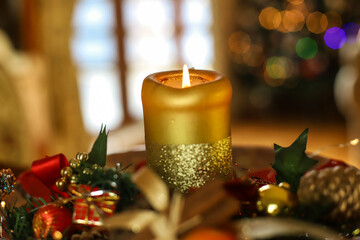 Świąteczna świeca z cynamonem, szyszkami, jabłkiem i innymi ozdobami na tle świątecznej świecącej choinki. Świąteczny nastrój © Anna